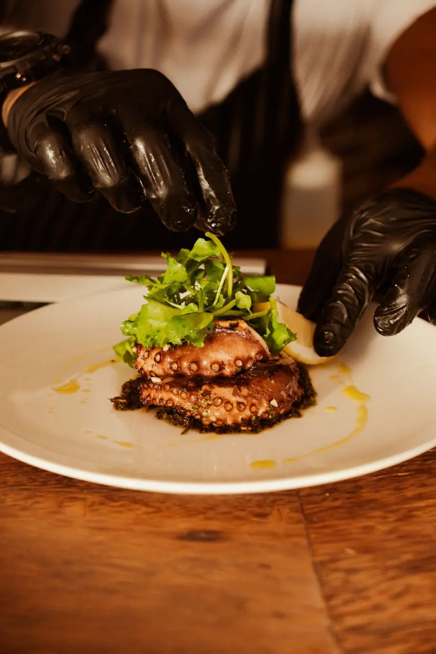 Chef garnishing plated seafood in professional culinary uniform